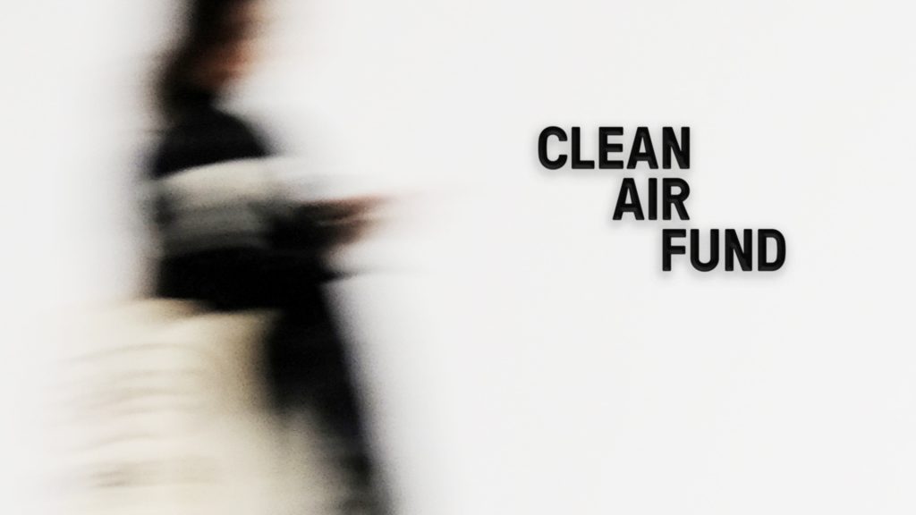 The Clean Air Fund logo as it would appear on a wall, with a person walking past.