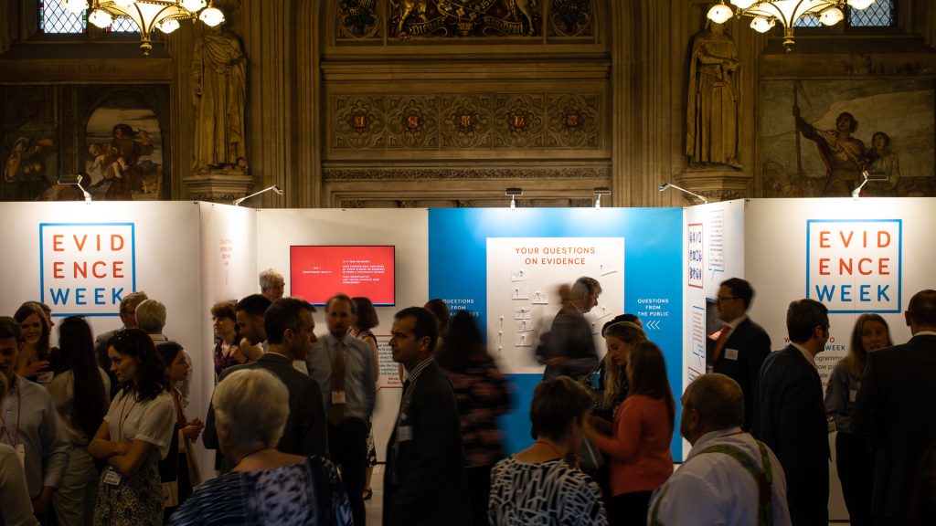 A crowd of people in front of the exhibition stand in the Upper Waiting Hall of the UK Parliament.