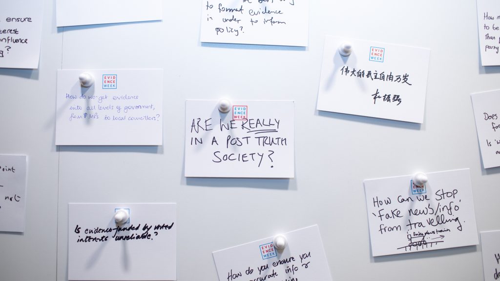 A white pin wall with attached hand written notes on the Evidence Week exhibition stand.