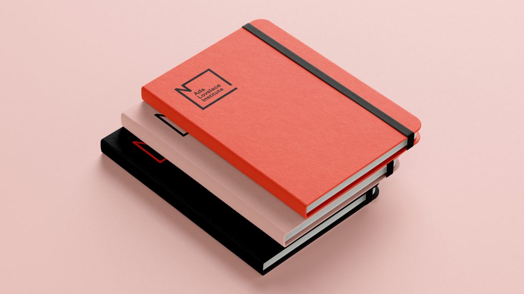 Stack of three notebooks with Ada Lovelace Institute logo in brand colours – orange, light pink and black.